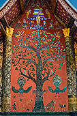 Wat Xieng Thong temple in Luang Prabang, Laos. Detail of the famous tree of life mosaic of the back wall of the sim, in colored glass on a dark red background. 